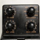 Černý kytarový efekt s čtyřmi ovládacími knoflíky. Na panelu jsou nápisy EQ. GAIN, FREQUENCY, OUT LEVEL a OVER DRIVE s doprovodnými stupnicemi čísel…