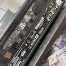 Zadní strana černého kytarového komba s kovovými ventilačními mřížkami. Na černém panelu je bílý nápis LINE 6 BigAmp a logo G1. V pravé části jsou um…