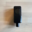 Černý mikrofon s obdélníkovým tvarem a kovovou mřížkou v horní části. Na spodním plastovém těle je viditelné označení CE. Nástroj leží na světlé dřev…