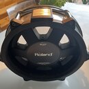 Černý elektronický buben s kovovými prvky. Uprostřed je bílý nápis Roland a nad ním označení modelu PD-125X DUAL TRIGGER PAD. V horní části je zlatý…