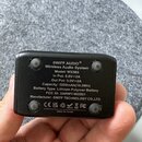 Fotografie zachycuje zadní stranu černého plastového zařízení. Na povrchu je bílý text: SWIFF AUDIO®, Wireless Audio System, Model: WX503, In Put: 5.…