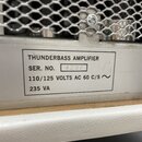 Detailní záběr na stříbrný kovový štítek s černým textem. Na štítku je nápis THUNDERBASS AMPLIFIER, SER. NO. 4237, 110/125 VOLTS AC 60 C/S s symbolem…