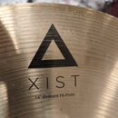 Detailní pohled na povrch mosazného činele. Na povrchu je černý trojúhelníkový symbol a pod ním nápisy XIST a 14" Brilliant Hi-Hats. Povrch vykazuje…