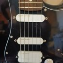 Detail elektrické kytary s černým lakem a černým pickguardem. Nástroj má tři bílé snímače, z nichž horní dva mají nápis „Fender Lace Sensor“ a spodní…