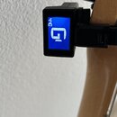 Černý digitální ladicí přístroj připevněný na hředelník dřevěného nástroje. Modrý displej zobrazuje bílé písmeno „G“ a v horním rohu nápis „440“. Zař…