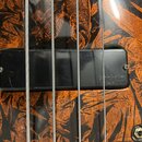 Detailní záběr na černý snímač basové kytary s nápisem bartolini mk1. Snímač je umístěn na těle nástroje s výraznou oranžovo-černou dřevěnou struktur…