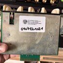 Fotografie zachycuje zadní stranu elektronického modulu s kovovým krytem a zeleným základním plošným spojem. Na kovovém krytu je bílá nálepka s nápis…