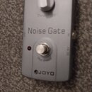 Stříbrný efekt pedál s nápisem Noise Gate a logem JOYO. Na horní části je bílý ovládací knoflík s popiskem Threshold a ve spodní části stříbrný spína…