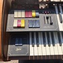 Detailní pohled na ovládací panel a klávesy elektronického orgánu v dřevěném korpusu. Panel obsahuje barevné přepínače s nápisy FLUTE 15', FLUTE 8',…