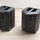 Dva černé plastové aktivní reproduktory s hranatým tvarem a úhlíkem nahoře pro umístění na stojan. Zadní panely obsahují ovládací prvky, konektory a…