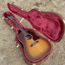 Akustická kytara s tělem typu dreadnought v barevném provedení sunburst, umístěná v otevřeném hnědém tvrdém pouzdře s červeným vnitřkem. Na hlavě nás…