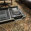Černý DJ mixážní stůl a přehrávač umístěné v hliníkovém transportním kufru. Na přehrávači je viditelné logo Pioneer a označení modelu CDJ-1000. Povrc…