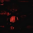 Fotografie zachycuje vnitřek zesilovače s několika zapnutými elektronkami, které vyzařují červené světlo. Na jedné z centrálních elektronek je vidět…