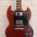 Elektrická kytara s červeně hnědým dřevěným povrchem a černým pickguardem. Nástroj má dva humbuckery, stříbrný most a čtyři ovládací knoflíky. Na hma…