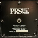 Detail zadní strany černého reproduktorového boxu s texturovaným povrchem. Na černé kovovédesce je bílé logo PRS PAUL REED SMITH a nápisy SPEAKER CAB…