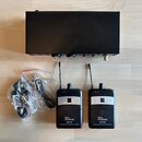 Černý bezdrátový systém pro in-ear monitoring. Sada obsahuje jeden hlavní vysílač a dva malé přijímače s anténami, z nichž oba mají bílý nápis „the e…