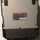 Zadní strana šedého efektového pedálu s černým rámem. Na stříbrném štítku je uveden nápis zoom ZOOM CORPORATION, Designed by ZOOM in Japan, Assembled…
