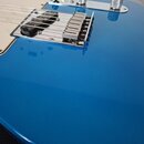 Detailní pohled na modrou elektrokitaru s lesklým povrchem. Je vidět jeden černý humbucker, chromovaný most a dva stříbrné oválné knofíky. Na těle ná…