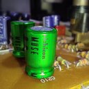 Detailní pohled na elektronickou desku s několika součástkami. V popředí jsou dva zelené válcové kondenzátory s nápisy MUSE a nichicon. Na desce jsou…