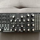 Stříbrný semi-modulární analogový syntetizátor s dřevěnou bočními stěnami. Na předním panelu je vlevo dole nápis SUBHARMONICON | SEMI-MODULAR ANALOG…