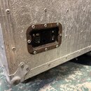 Detail stříbrného transportního kufru z texturovaného materiálu s kovými hranami a rohy. V bočnici je osazený černý konektorový panel s třemi vstupy,…