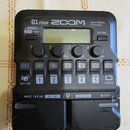 Černý multi-efektový procesor s nápisy G1 FOUR, ZOOM a Multi-Effects Processor. Zařízení obsahuje displej, čtyři ovládací knoflíky s popisky Lo, Mid,…