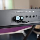 Detail zadní strany černého klavírního nástroje s připojenými dvěma moduly WIDI Master. Na panelu jsou viditelné nápisy MIDI OUT, MIDI IN, FOOT PEDAL…