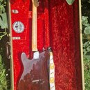Elektrická kytara typu Telecaster s tmavě hnědým průhledným lakem těla a světlým dřevěným hmatníkem. Nástroj leží v otevřeném kufru s červeným plyšov…