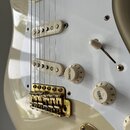Detail elektrické kytary v krémové barvě s bílým pickguardem. Nástroj má tři bílé snímače typu single-coil a zlatý kobylník. Na bílých oválných knofl…