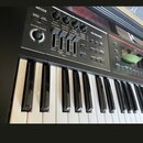 Detailní pohled na ovládací panel a klávesnici černého elektronického nástroje. Na panelu jsou nápisy MODE, KEYBOARD, MASTER VOLUME a řada posuvníků…