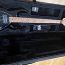 Černá elektrická basová kytara v černém tvrdém kufru. Na hlavě nástroje je viditelné logo Schecter. Hmatník a krk jsou vyrobeny ze světlého dřeva. Po…