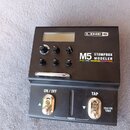 Černý kytarový efekt s nápisy LINE 6 a M5 STOMPBOX MODELER. Pod názvem modelu je seznam efektů: DELAY | MOD | DISTORTION | FILTER | VERB. Zařízení má…
