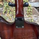 Detail zadní strany hřdelníku a spoje krku s tělem hnědé elektrické kytary. Na kovové spojovacídesce je vyražené logo Epiphone a pod ním nečitelný te…