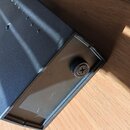 Černý kovový box s hranatým tvarem. Na boční straně je umístěn jeden křížový šroub a v horní části jsou vidět malé otvory. Z horní části zařízení vyv…