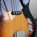 Detail elektrické basové kytary s tělem v barevnosti sunburst a černým pickguardem. Na snímači je viditelný nápis Glaswell. Nástroj má chromovaný kry…
