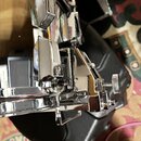 Detailní záběr na chromovaný obruč a napínací mechanismus bubnu. Na kovových prvcích jsou vidět odrazy okolí a drobné nečistoty. Žádné značky, loga a…