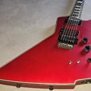 Červená elektrická kytara s atypickým, ostře hranatým tvarem korpusu. Nástroj má dva humbuckery, jeden ladicí most a tři ovládací knofíky s přepínače…