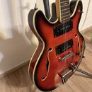 Polodupatá elektrická kytara s červeně-černým přechodem (sunburst) a krémovým lemováním. Nástroj má dva černé humbuckery, dvě f-otvory a kovový most…