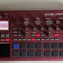 Bordeaux červený sampler KORG electribe sampler MUSIC PRODUCTION STATION. Zařízení obsahuje displej s nápisem 001 Advisory 1 Part:01 OSC: Trap, někol…