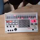 Bílý sampler s ovládacími prvky, tlačítky a červenými LED diodami. Na pravé straně je červený digitální displej s nápisem 71UE a značka KORG volca sa…