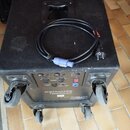 Černý aktivní subwoofer na čtyřech kolečkách s integrovanou rukojetí. Na zadním panelu je nápis DYNACORD PowerSub 212 a ovládací prvky s různými kone…
