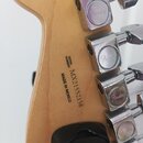 Detail zadní strany hlavy kytary z přírodního dřeva. Je zde vyryto „SERIAL NUMBER MX21552158“ a nápis „MADE IN MEXICO“. Na chromovaných kolébkách lad…
