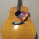 Akustická kytara s přirozeným dřevěným povrchem korpusu a tmavým hmatníkem. Na těle kytary leží obal s nápisy Elixir, ACOUSTIC, NANOWEB a 12 56. Nást…