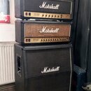 Sada kytarového komba značky Marshall v černém provedení, složená ze dvou zesilovačů a jednoho reproduktorového boxu. Všechny tři části mají bílý lem…