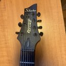 Černá hlava elektrické kytary s nápisem Schecter v horní části. Na straně je svisle napsáno DIAMOND SERIES® a níže v rámečku DAMIEN-7. Nástroj má sed…