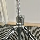 Detail chromovaného stojanu z kovu s teleskopickým mechanismem a viditelným závitem. Stojan má tříramennou základnu a v dolní části je umístěn utahov…
