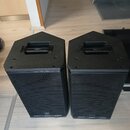 Dva černé reproduktory s kovovými mřížkami a úhlovým provedením horní části. Na horních úchytkách je nápis SERIES a v dolní části čelních mřížek se n…