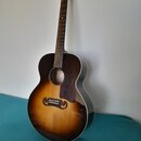 Akustická kytara s korpusem v barevném přechodu od tmavě hnědé k žluté (sunburst). Nástroj má tmavý hmatník a bílý lem kolem korpusu. Na hlavě krku j…