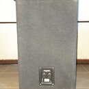 Zadní strana šedého reproduktorového boxu potaženého látkou. V horní části je umístěn černý kontrolní panel s konektory, ventilátorem a nápisy OUTPUT…