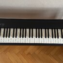 Černá digitální pianola na černém stojanu. Na pravé straně korpusu je bílý nápis Roland a pod ním model FP-30X. Na levé straně jsou umístěna ovládací…